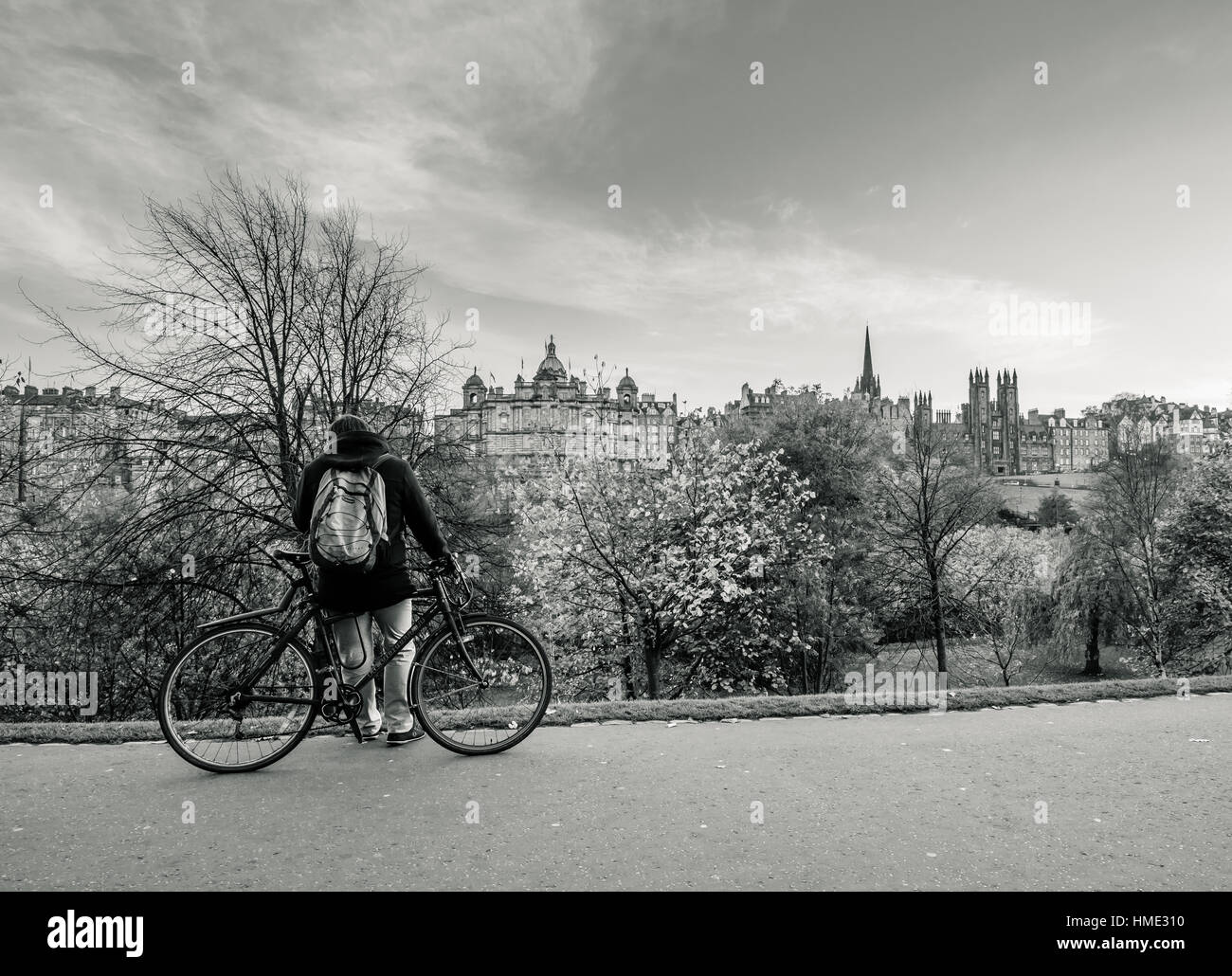 Un homme tenant un vélo dans les jardins de Princes Street à Edimbourg avec une vue vers la gare de Waverley et de la vieille ville (en noir et blanc) Banque D'Images
