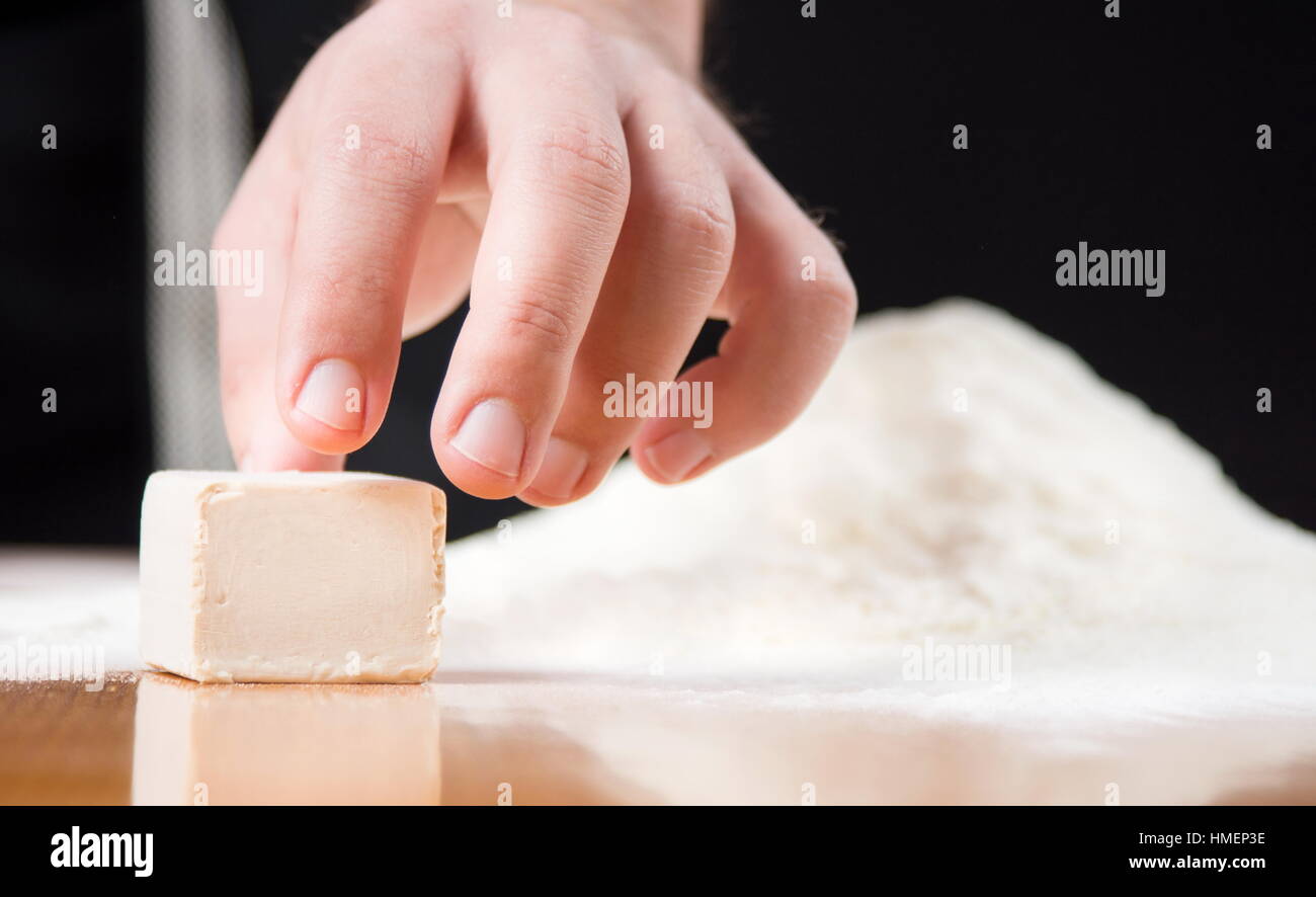 Main mâle atteignant cube de levure de boulangerie sur un tableau Banque D'Images