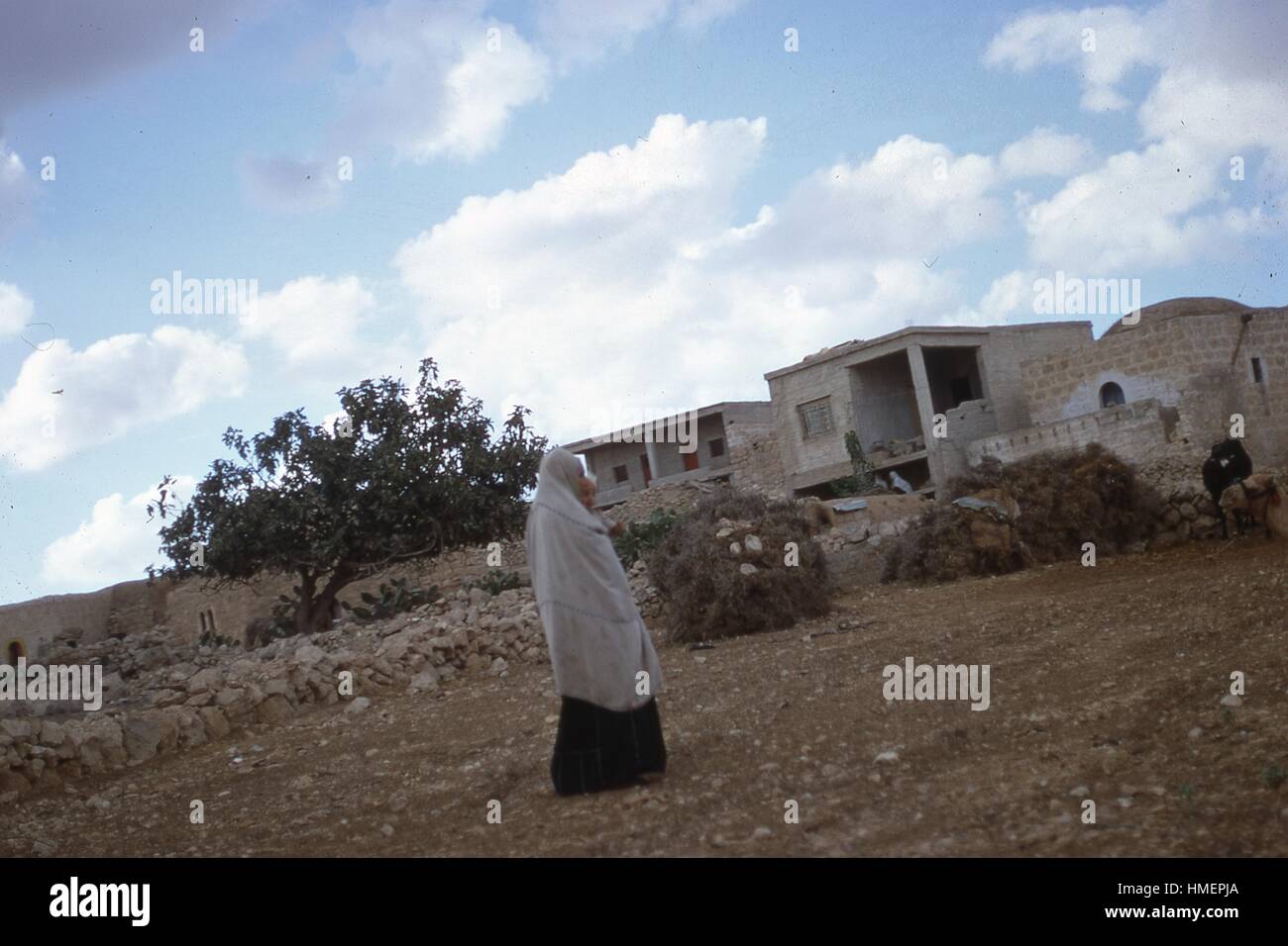 Femme arabe portant un niqab ou burqa porte un enfant tout en marchant sur des terres rocheuses vers les maisons et bâtiments en arrière-plan, à Hébron, Israël, Novembre, 1967. (Photo de la Collection Morse/Gado/Getty Images). Banque D'Images