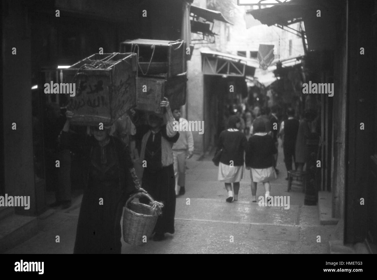 Scène qui se déroule dans le quartier arménien de femmes portant de grandes boîtes de produire sur leurs têtes, dans la vieille ville de Jérusalem, Israël, Novembre, 1967. Les écolières en uniforme à pied en bas de l'escalier du couloir de la rue à l'arrière-plan. (Photo de la Collection Morse/Gado/Getty Images). Banque D'Images