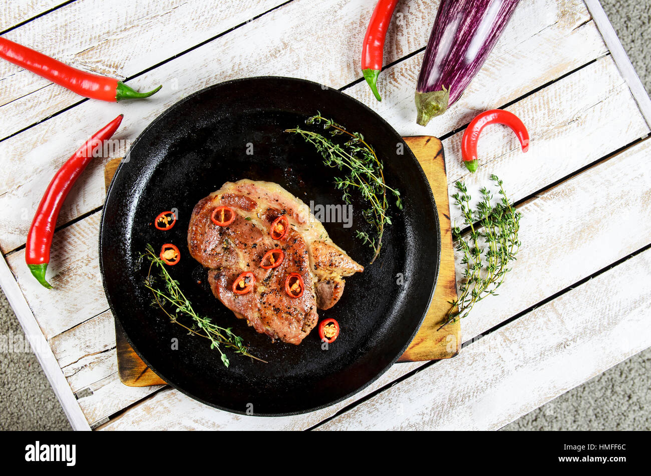 La viande avec les épices dans une casserole, romarin, et Hot Chili Peppers sur un arrière-plan de table en bois blanc Banque D'Images