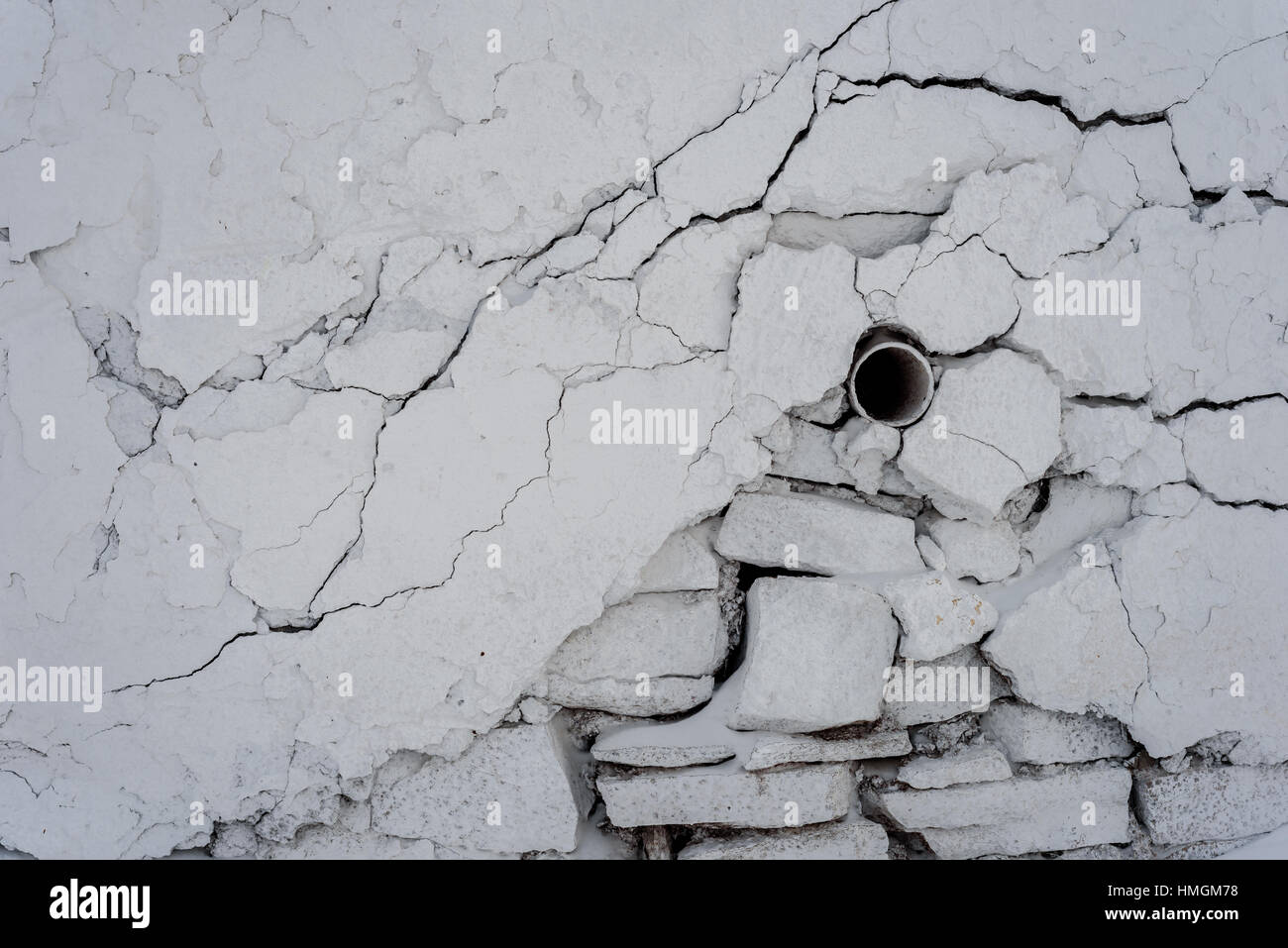 Tuyau d'eau unique qui dépasse de la fissuration d'un mur de plâtre blanc avec des fissures de surface et les fissures. Banque D'Images