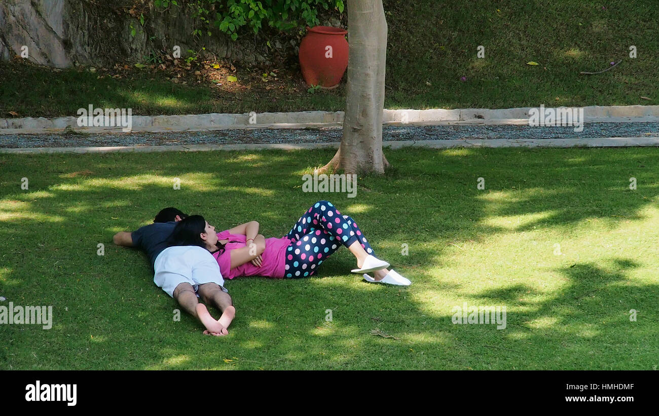 Un couple de détente sur la pelouse dans un jardin, l'homme couché à l'envers, la femelle faisant de lui un oreiller, vacances à un resort Banque D'Images