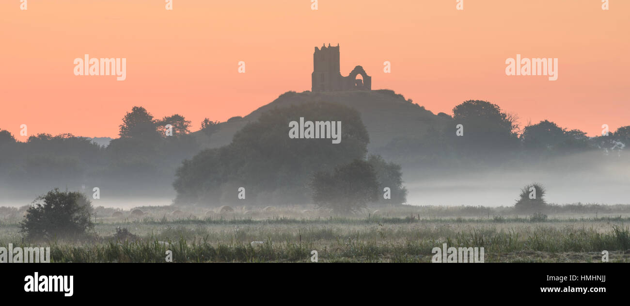 Burrow Mump silhouetté contre un ciel aube dynamique sur un matin brumeux sur les niveaux de Somerset. Banque D'Images