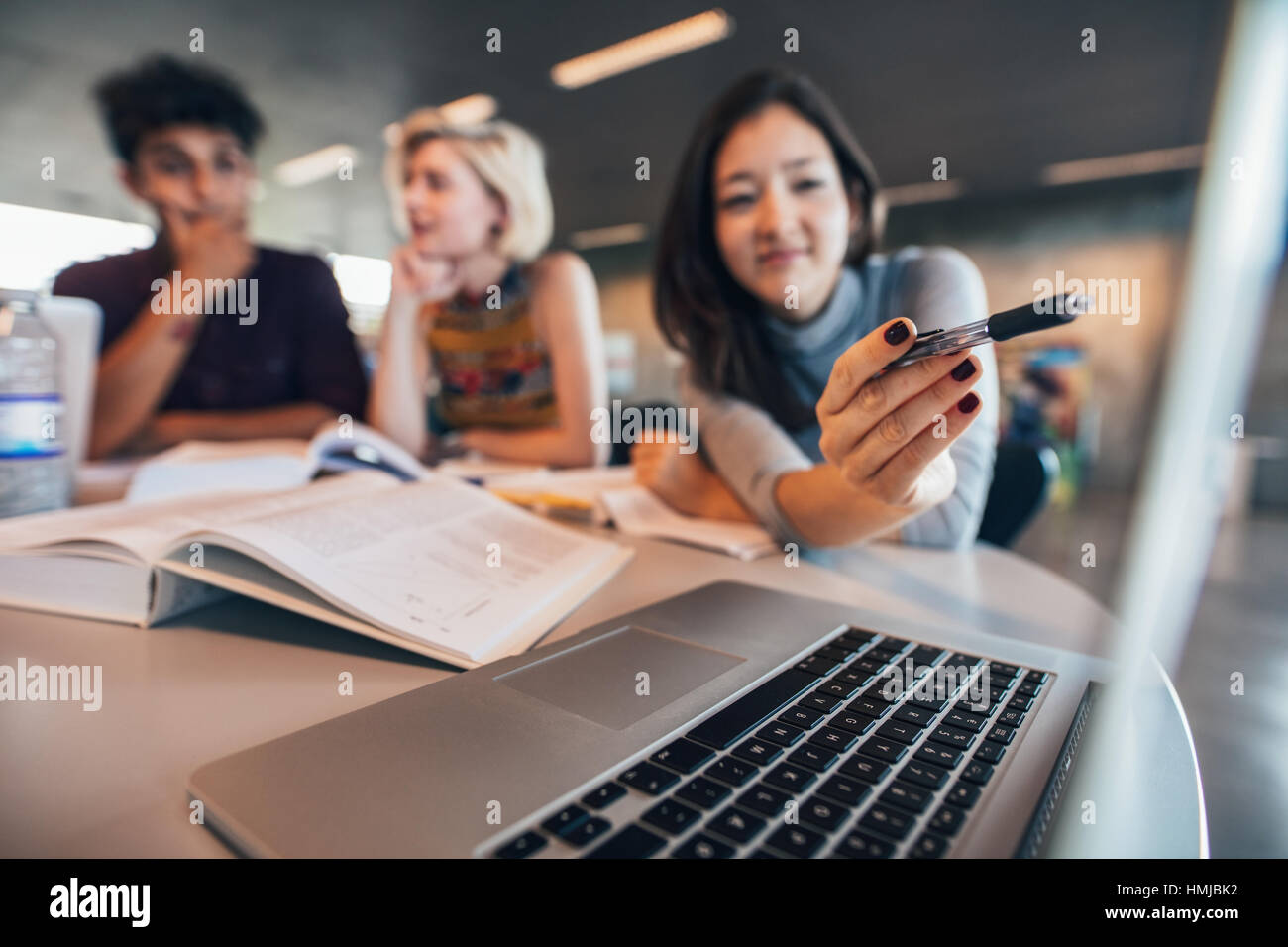 Groupe d'étudiants universitaires travaillant sur l'ordinateur portable dans une bibliothèque avec femme pointant sur l'écran du portable. Banque D'Images