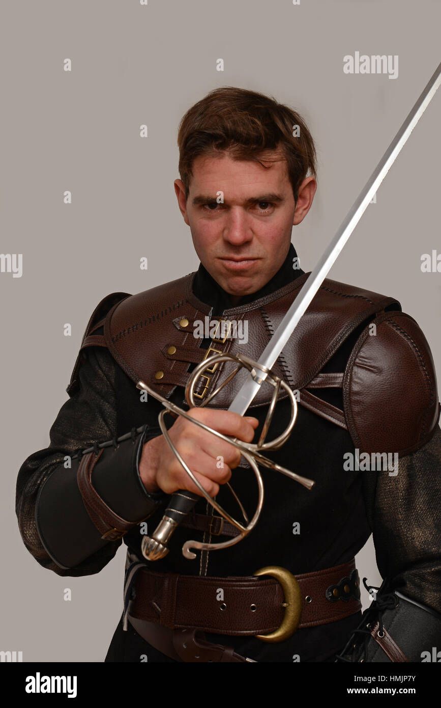 Un acteur en costume grimaces tout en tenant son épée contre un arrière-plan gris Banque D'Images