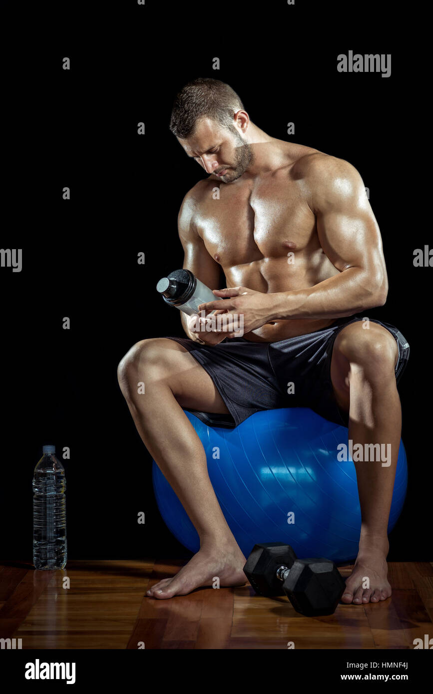 Young adult man drinking protein shake en salle de sport. Fond noir. Banque D'Images