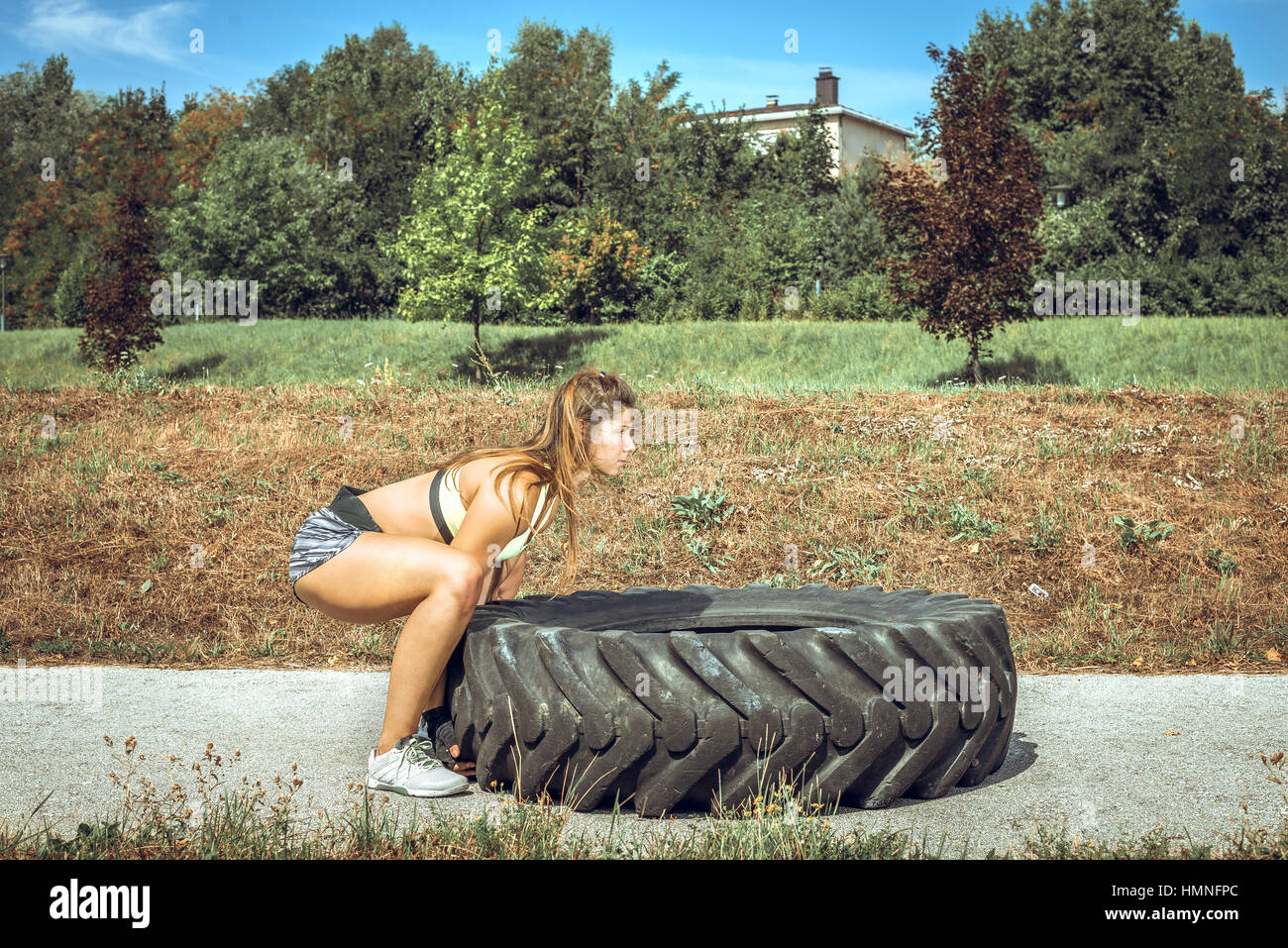 Young adult woman flipping et le matériel roulant au cours de l'exercice crossfit pneu à l'extérieur. Banque D'Images