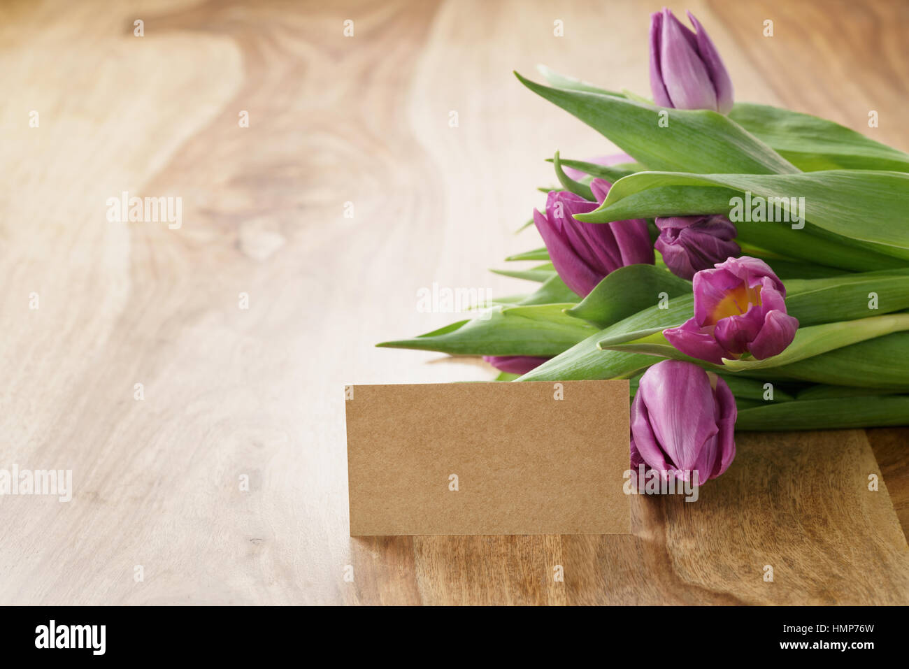 Bouquet de tulipes violettes sur table en bois avec une carte papier vide Banque D'Images