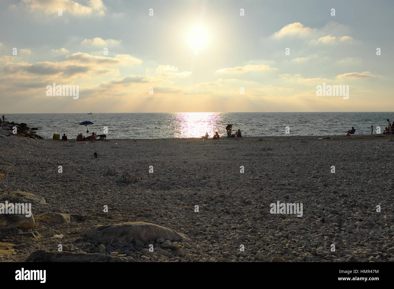 Attendre que le soleil à l'ensemble - Les personnes en attente de coucher du soleil à l'heure d'or dans une plage de galets à Marina di Pisa, Toscane, Italie, Europe Banque D'Images