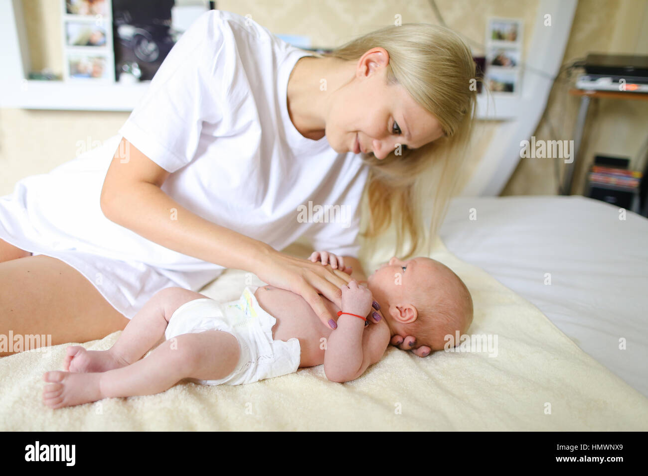 Jeune Mere Detient La Tete De Bebe Et Ne Massage Joue Et Chante Des Chansons Pour Enfant Qui Allonge Sur Un Lit Blanc En Couche Sur Couche Jaune Dans La Salle Lumineuse