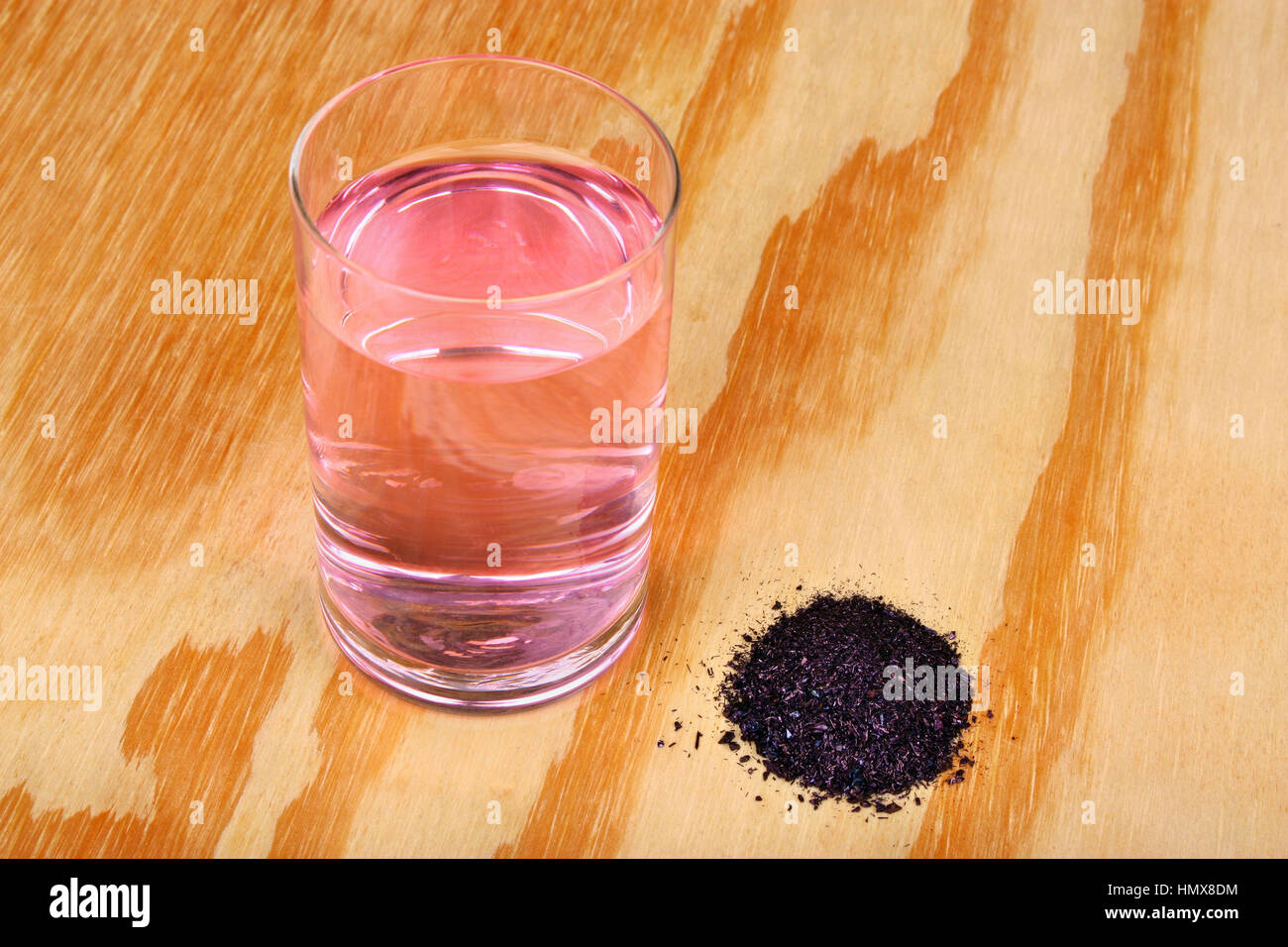 Amas de cristaux de permanganate de potassium et l'eau d'un verre sur une table en bois Banque D'Images