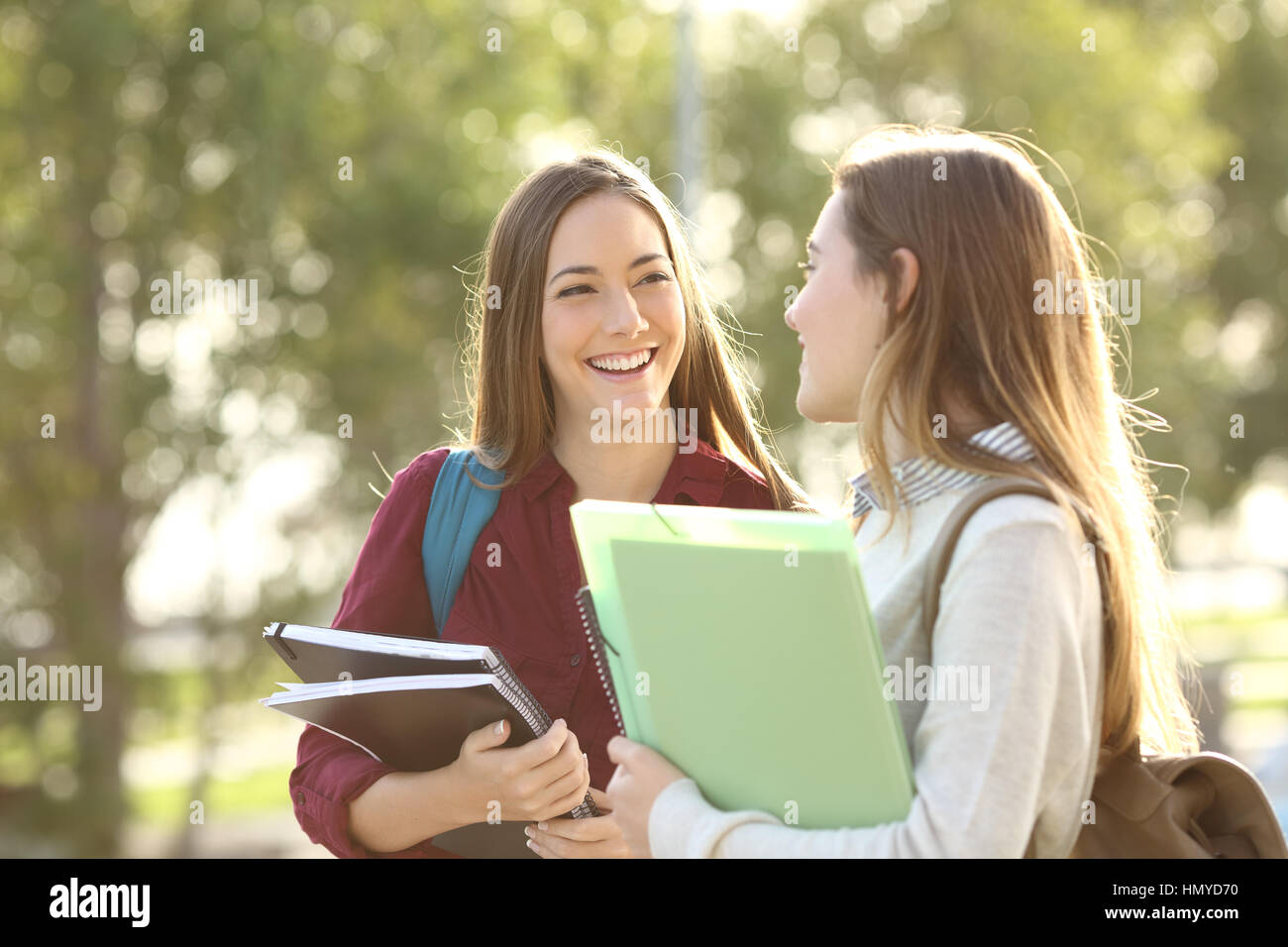 Deux étudiants heureux marcher et parler les uns les autres dans un campus au coucher du soleil avec une lumière chaude Banque D'Images