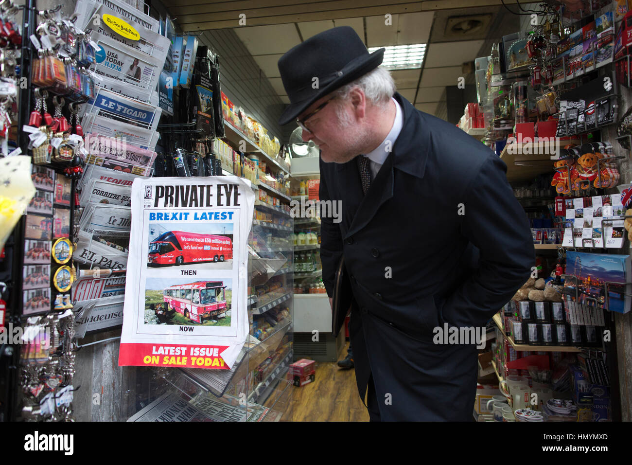 Homme portant un chapeau trilby s'arrêter pour regarder une copie de "Private Eye" magazine dans un kiosque à Londres, Victoria, England, United Kingdom Banque D'Images