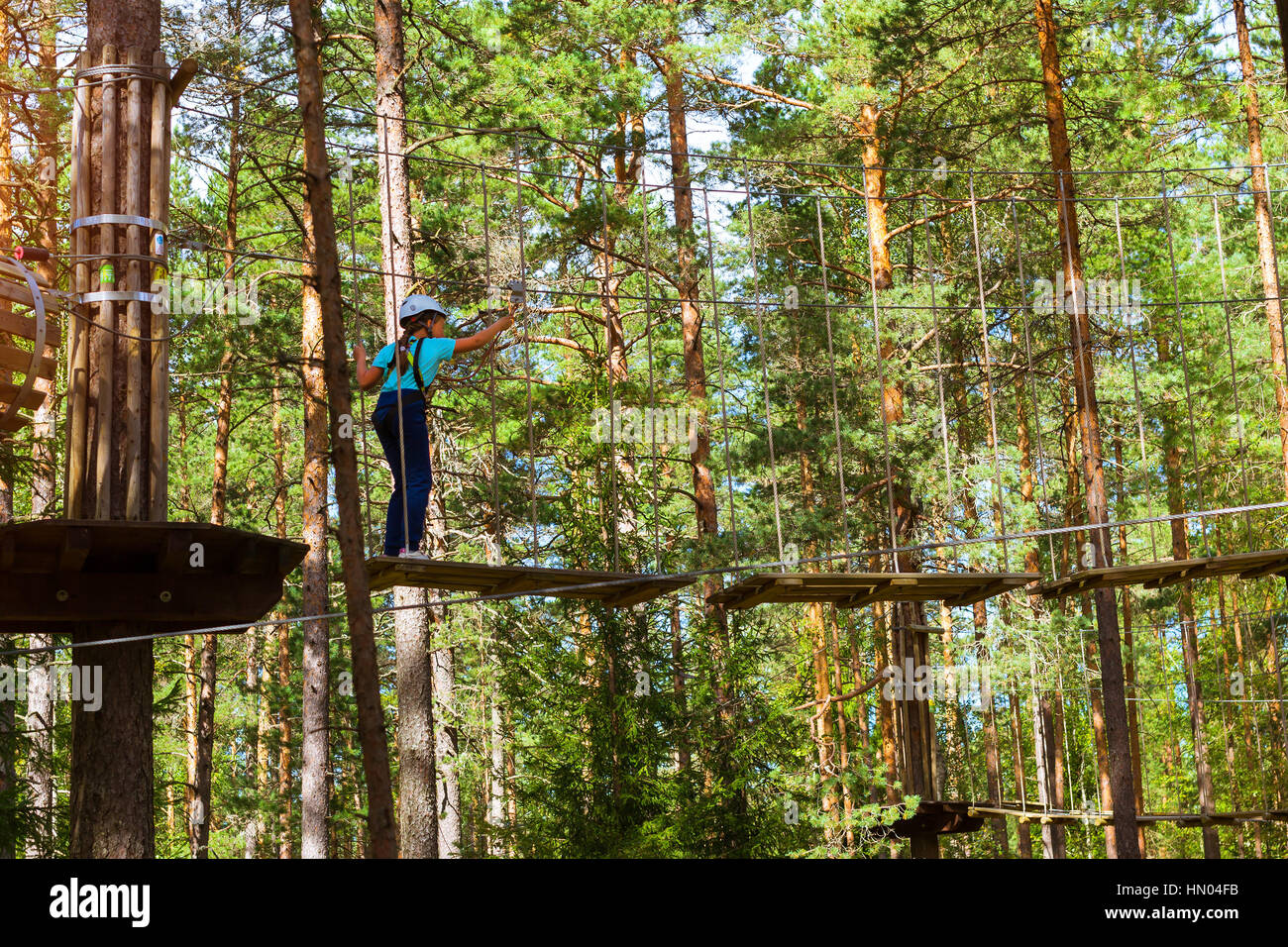 Adolescente poursuit en sentier à charnière dans l'extrême parc en forêt de l'été. L'escalade de haute altitude de la formation sur l'enfant parcours aventure, équipé de sa Banque D'Images
