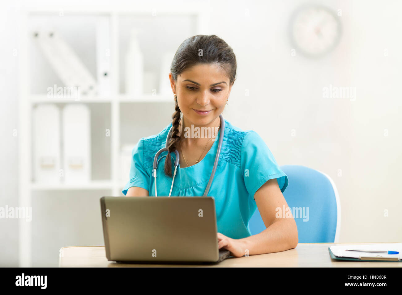 Smiling woman doctor using laptop sitting at desk in medical office Banque D'Images