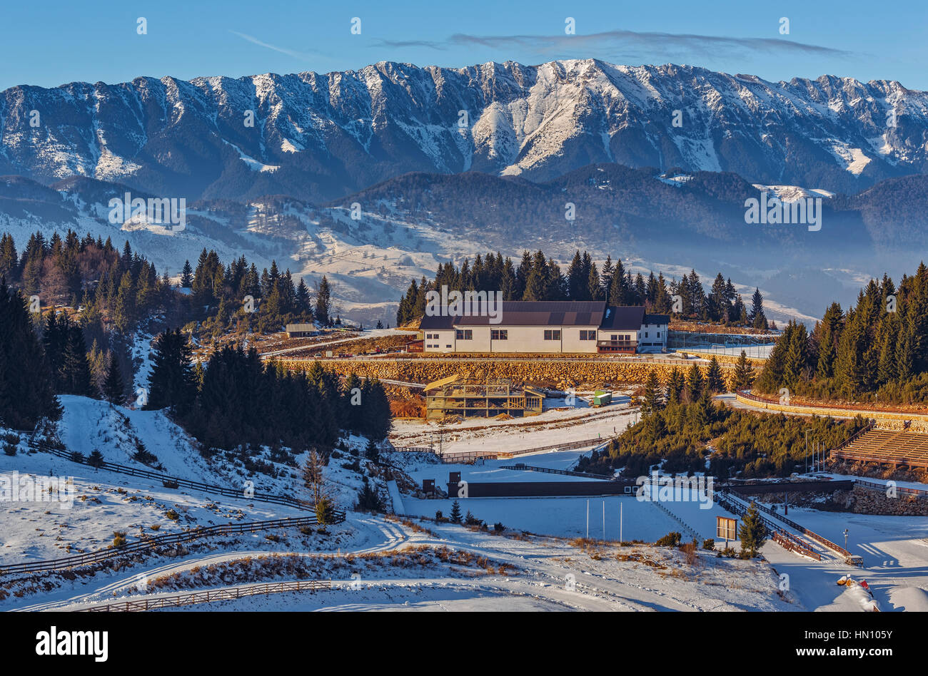Vue panoramique sur la station de ski touristique Fundata Aparthotel Gallahaus et les majestueuses cimes enneigées Piatra Craiului, Roumanie. Banque D'Images