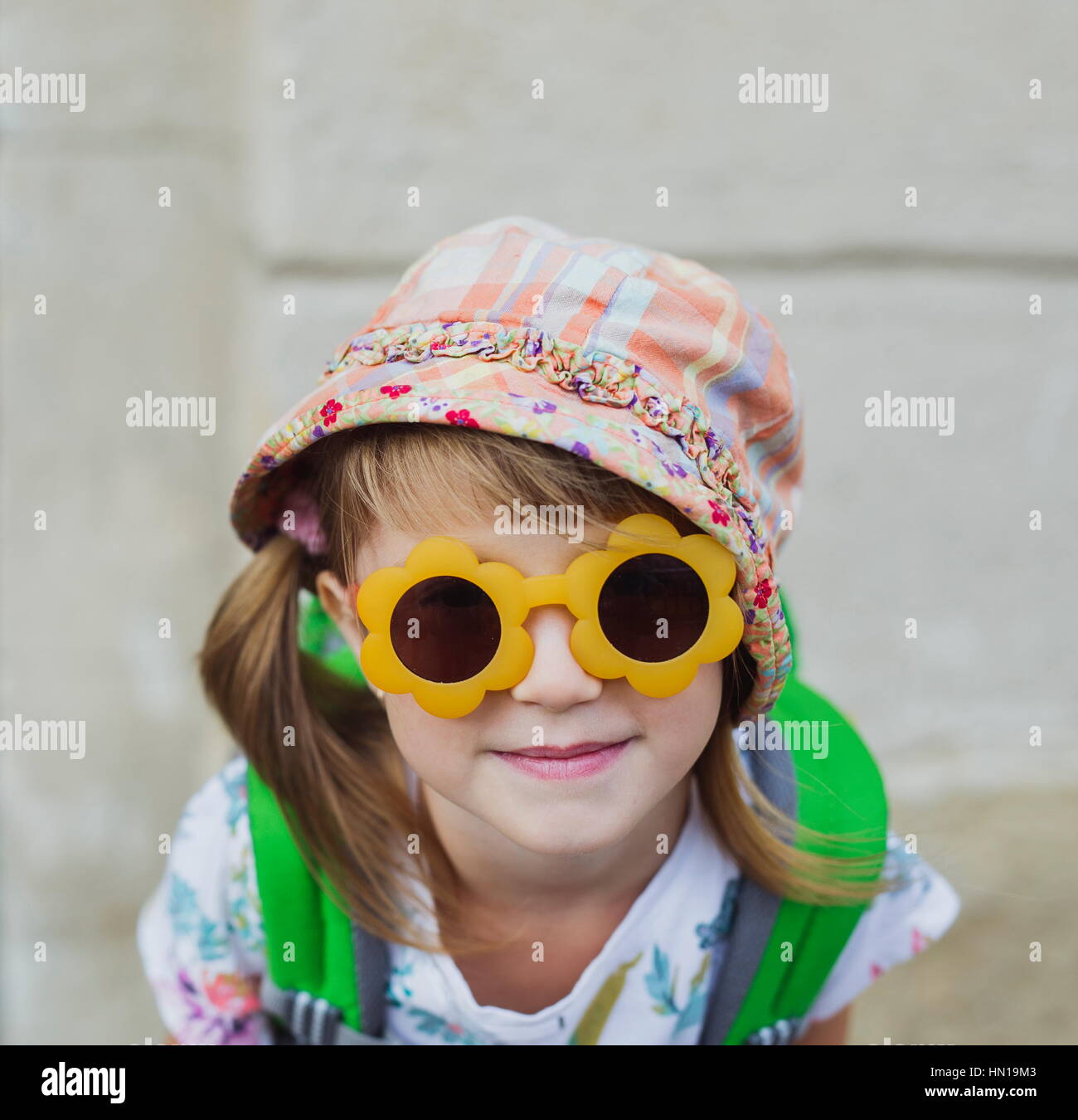 Cute smiling happy little girl avec un sac à dos, assis sur un banc. L'enfant dans la grande vieille ville. Lunettes de soleil enfant pendant les vacances d'été. Heureux litt Banque D'Images