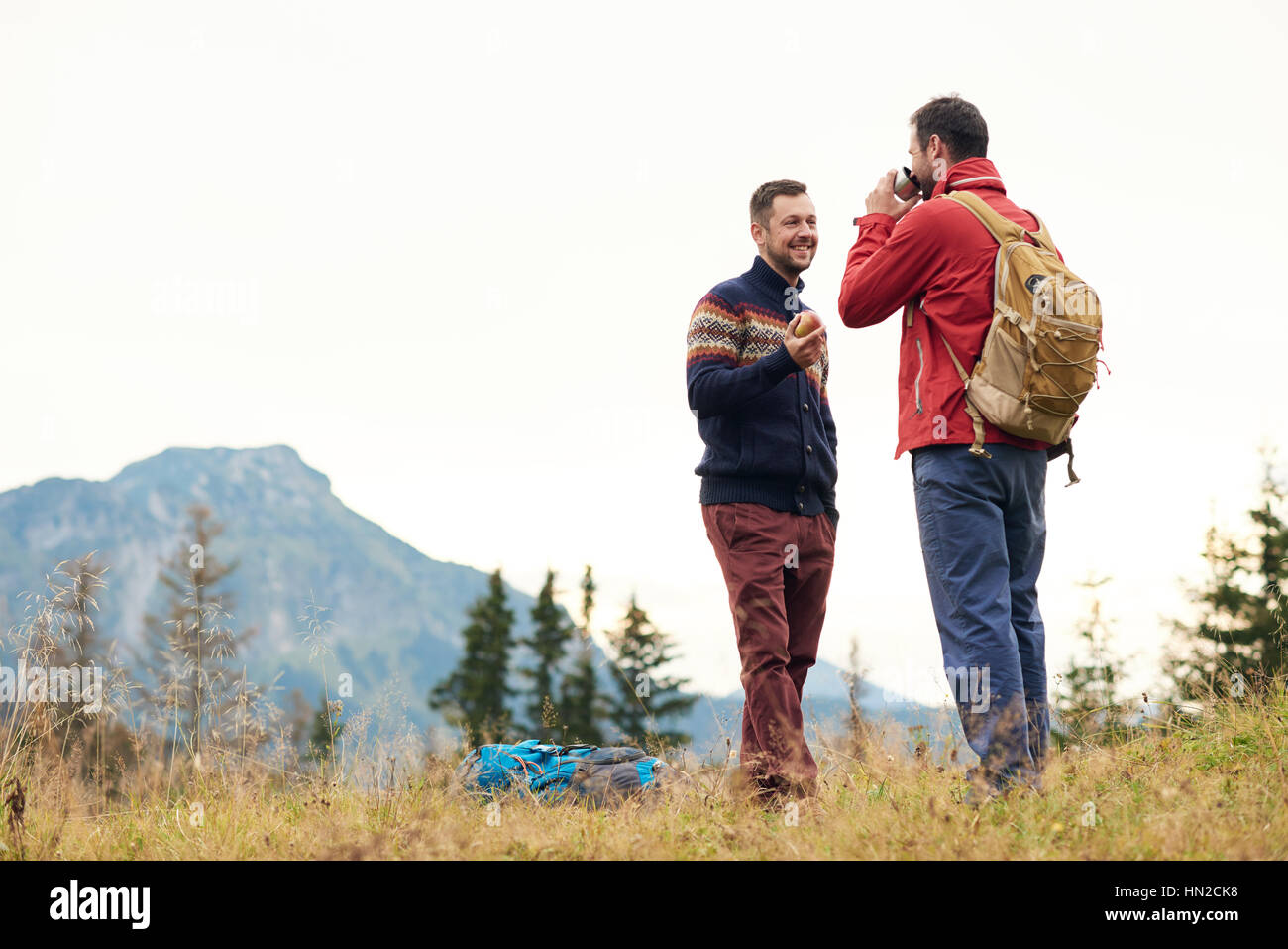 Deux jeunes hommes souriants en parlant ensemble d'équipement de randonnée tout en prenant une pause de trekking dans les montagnes Banque D'Images