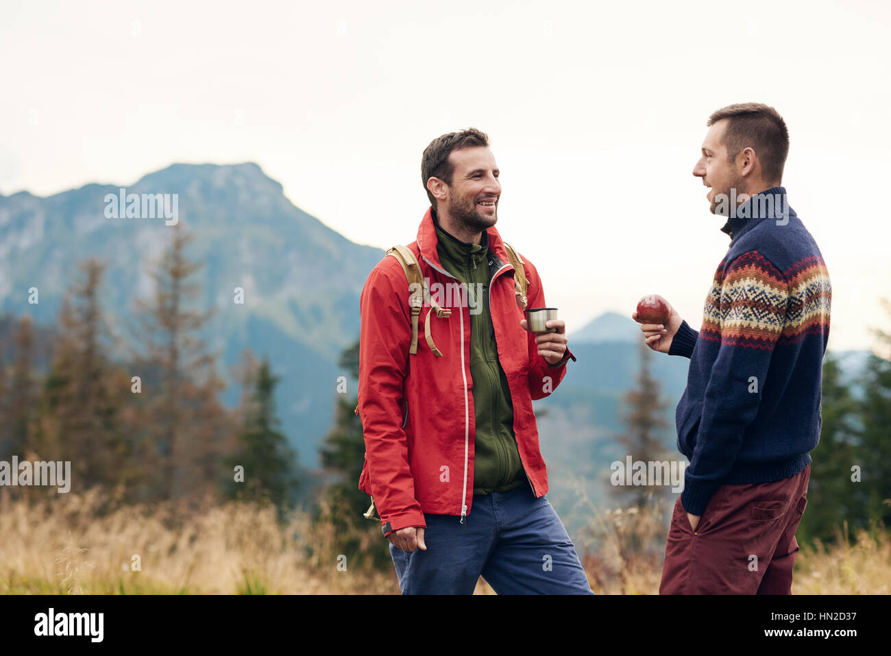 Deux jeunes hommes souriants en parlant ensemble d'équipement de randonnée tout en prenant une pause de trekking dans les montagnes Banque D'Images