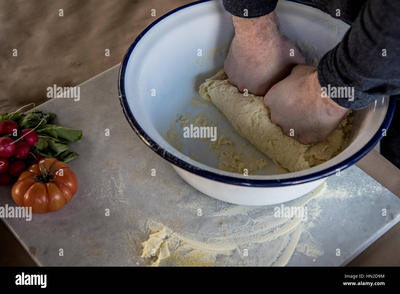Mains d'une personne dans un bol de pâte à pétrir sur planche à découper sur la table de marbre Banque D'Images