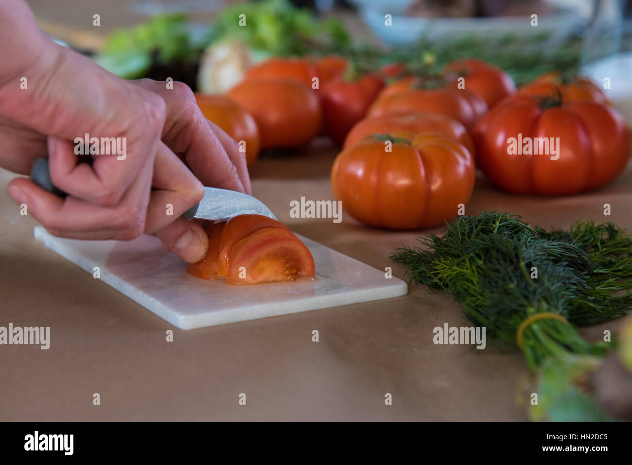 Mains tenant un couteau de trancher une tomate avec d'autres produits alimentaires frais en arrière-plan Banque D'Images