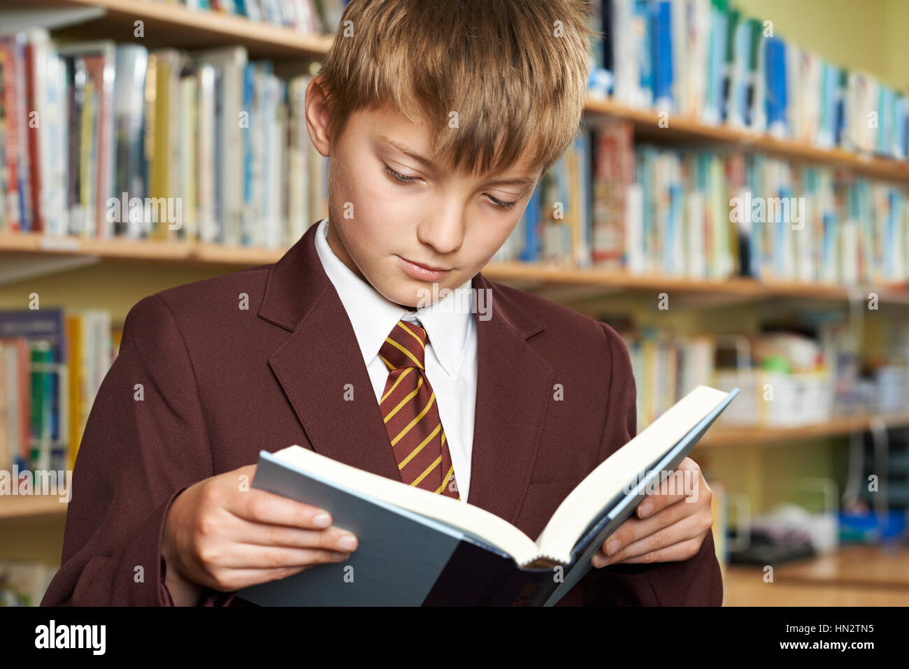 Boy Wearing School Uniform Reading Book in Library Banque D'Images