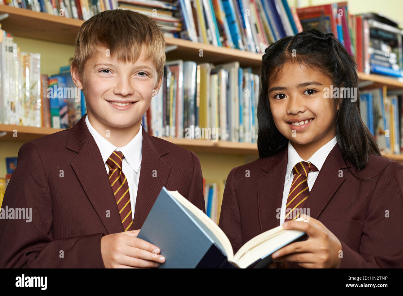Les élèves portant des uniformes scolaires Reading Book in Library Banque D'Images