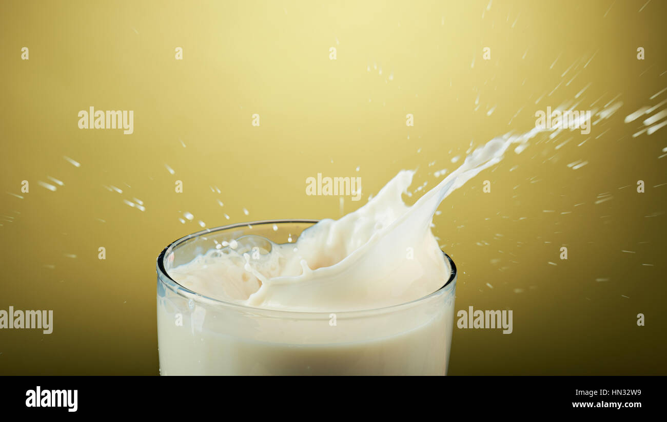 Close up of splash de lait en verre isolé sur fond jaune Banque D'Images
