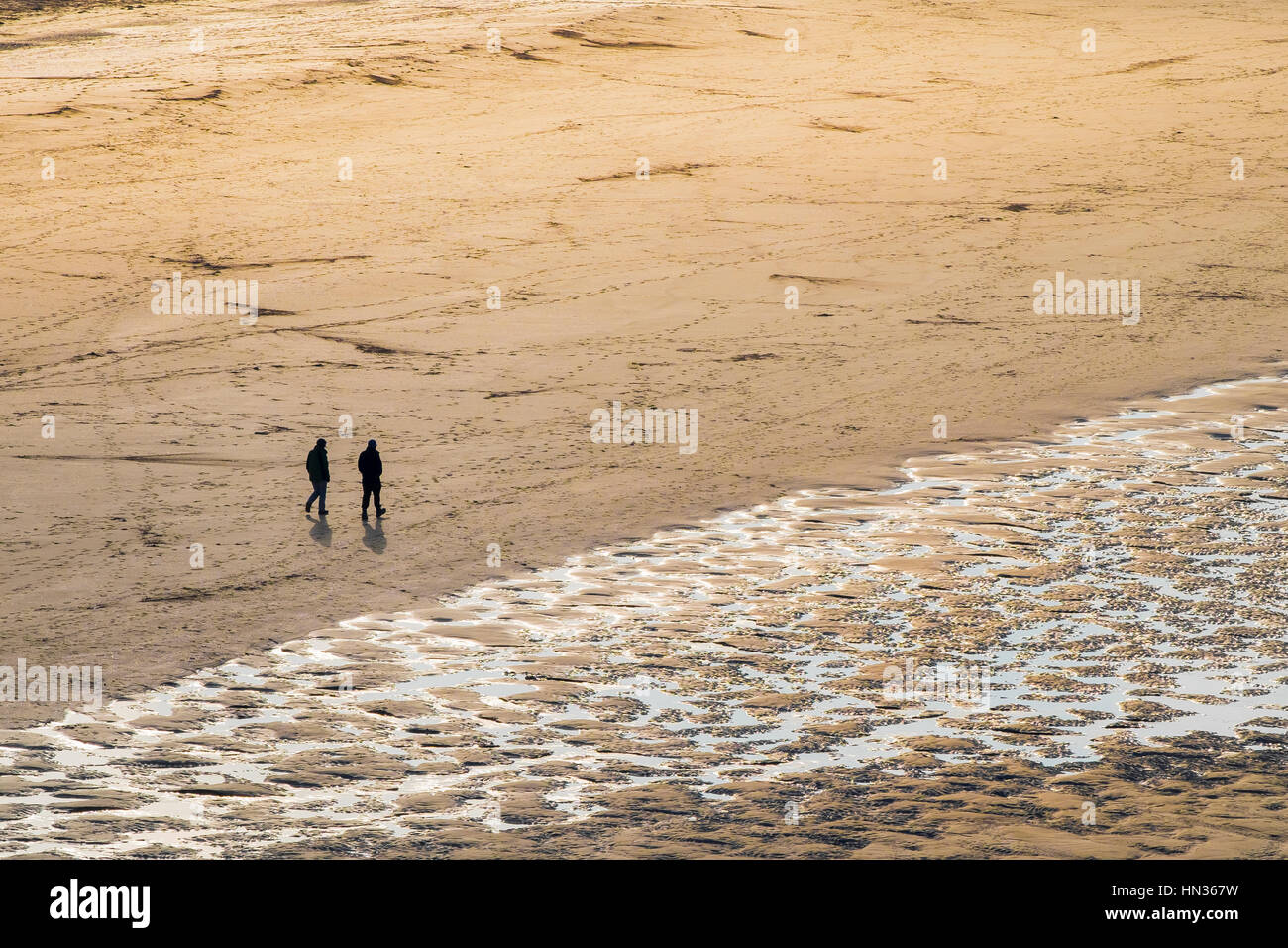 Deux personnes vu en silhouette et à distance sur la plage de Crantock à Newquay en Cornouailles. Banque D'Images