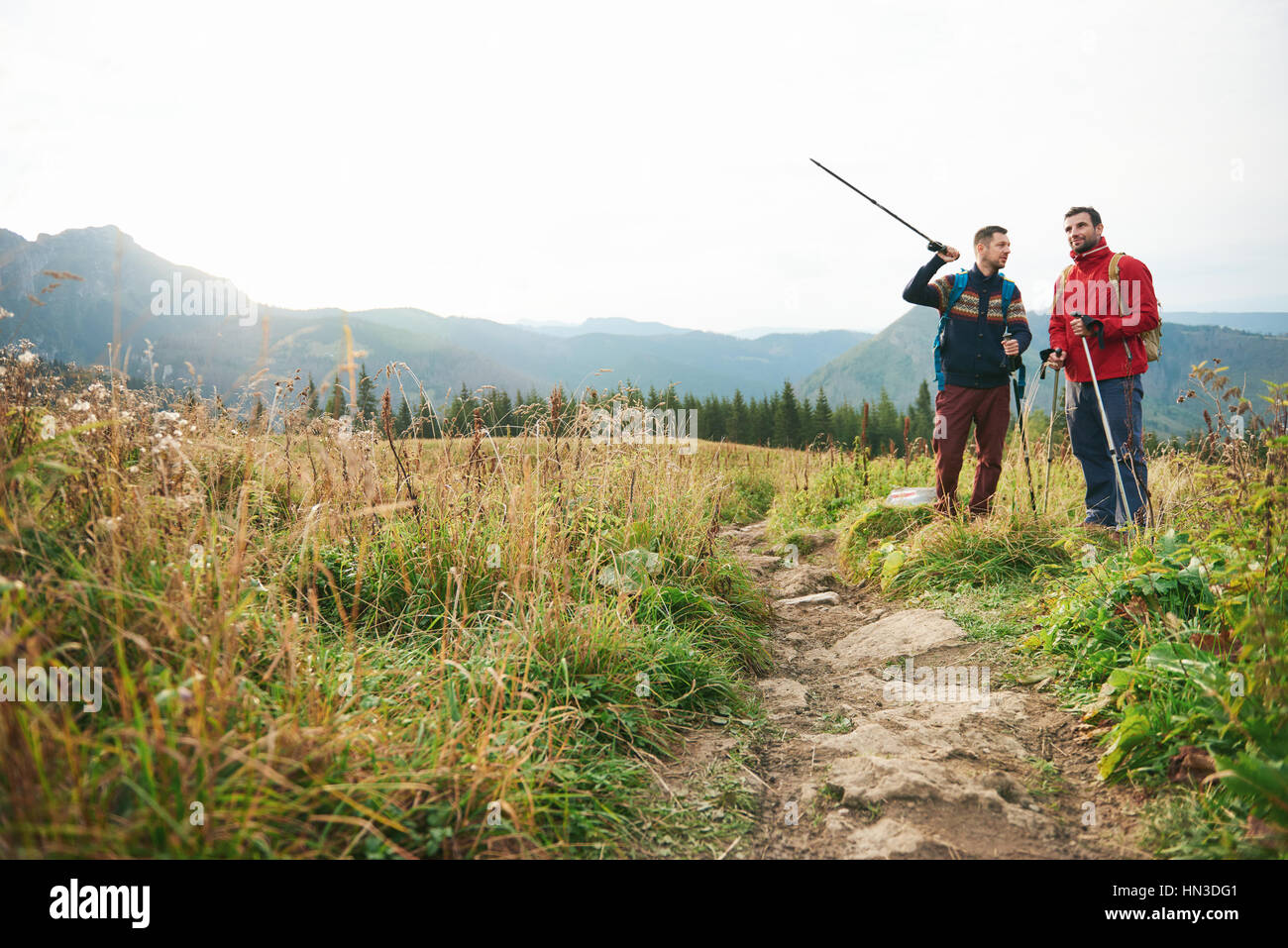 Deux jeunes hommes portant des sacs à dos et bâtons de marche de parler ensemble sur un sentier lors d'une randonnée dans les collines Banque D'Images