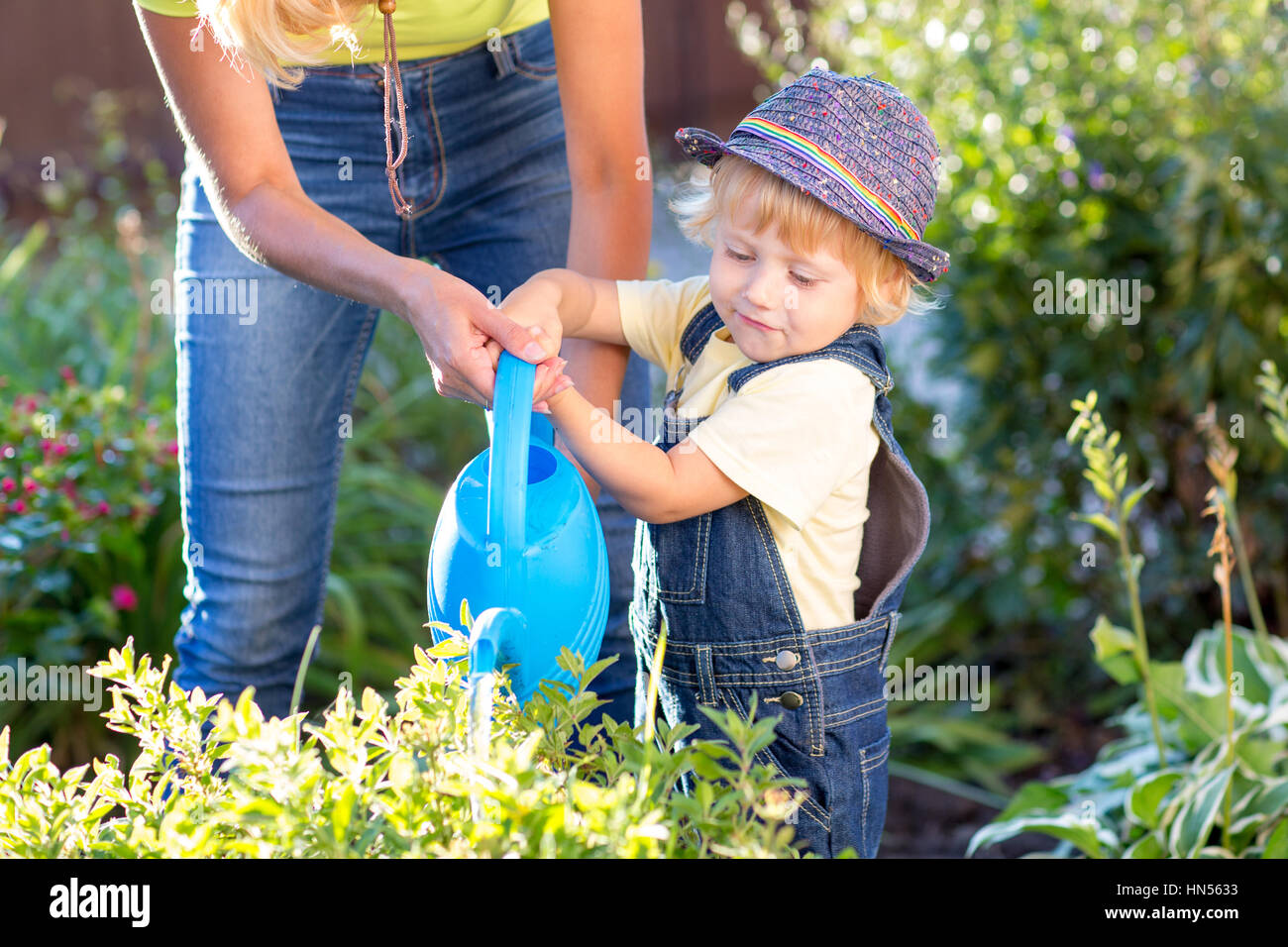 Kid avec maman travaillant dans le jardin. Arrosage des fleurs de l'enfant. Mère peu de fils. Banque D'Images
