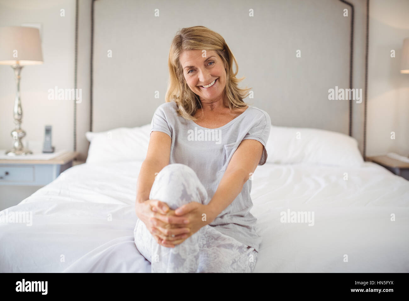 Portrait of smiling women assis les jambes croisées sur le lit chez lui Banque D'Images