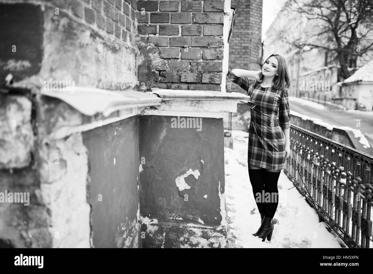 Une piscine portrait d'une jeune jolie fille aux cheveux rouges portant robe à carreaux avec girly sacs à dos debout sur le mur de brique en hiver d'arrière-plan Banque D'Images