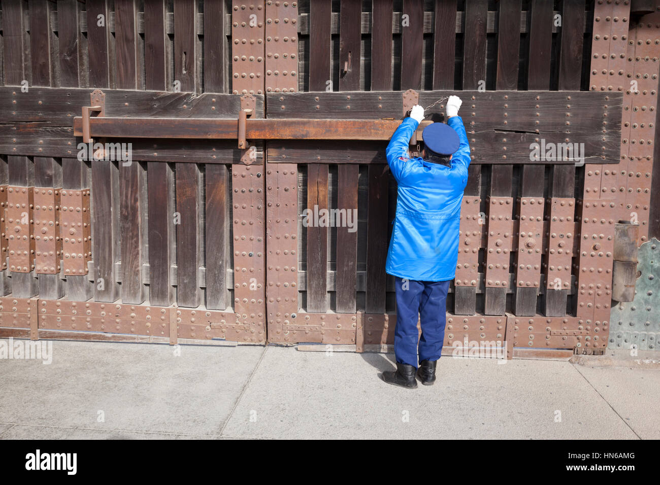 Kyoto, Japon - 19 mars 2012 : un gardien de sécurité dans un uniforme bleu verrouille la grande porte d'entrée pour le château de Nijo à Kyoto, au Japon. Banque D'Images