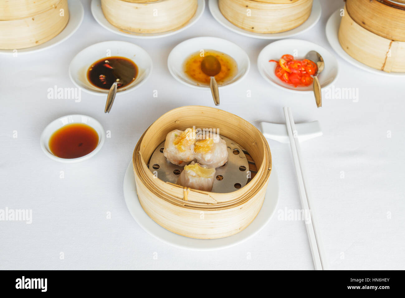 Dim sum crevettes Dragon eye alimentaire dumpling har gow dans panier de bambou au restaurant avec de la sauce soja, la sauce sucrée, sauce chili et baguettes. Banque D'Images