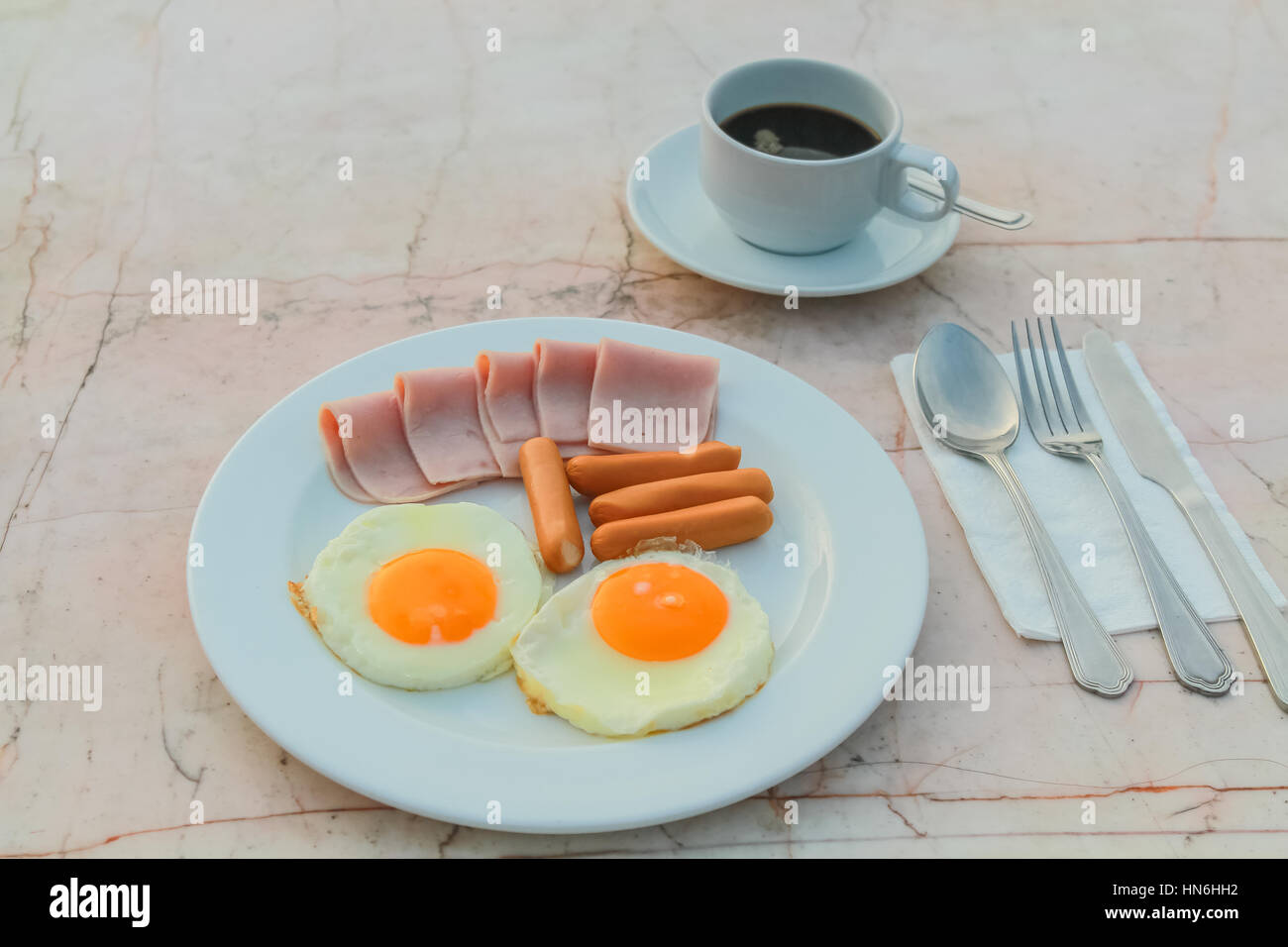 Le petit-déjeuner avec des oeufs frits, jambon, saucisses et du café noir sur la table de marbre. Banque D'Images