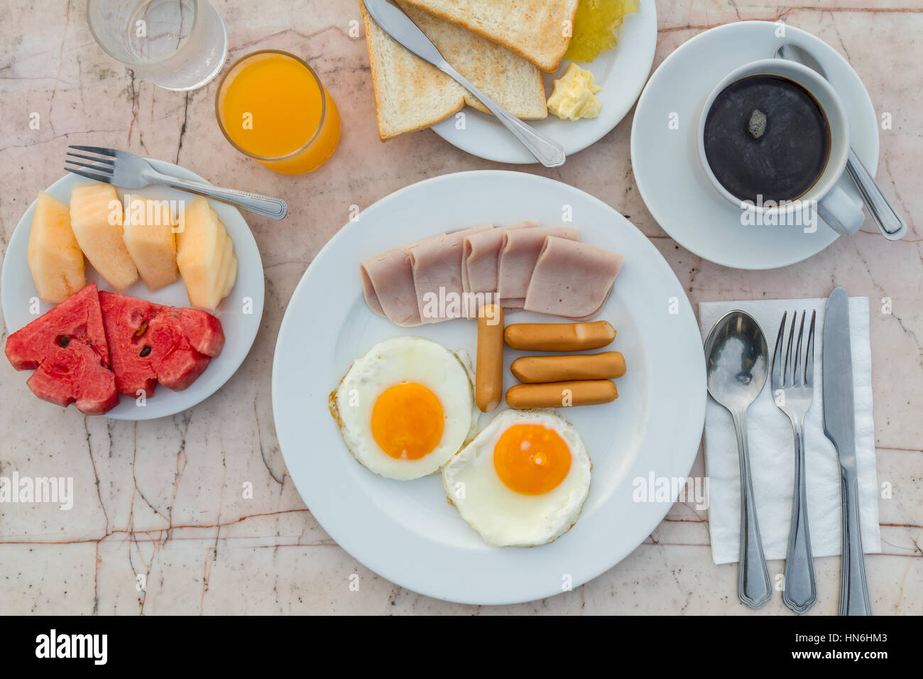 Le petit-déjeuner avec des oeufs frits, jambon, saucisses, pain grillé, de confiture, de beurre, de pastèque, jus d'orange et du café noir sur la table de marbre. vue d'en haut. Banque D'Images