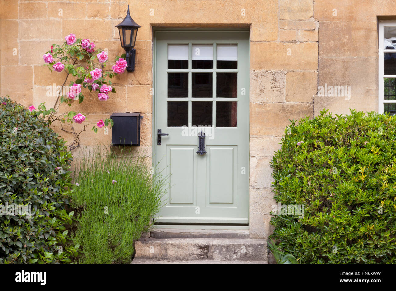 Portes en bois vert clair dans une vieille maison en pierre de chaux traditionnel anglais entouré de roses roses grimpantes, lavande, sur journée d'été Banque D'Images