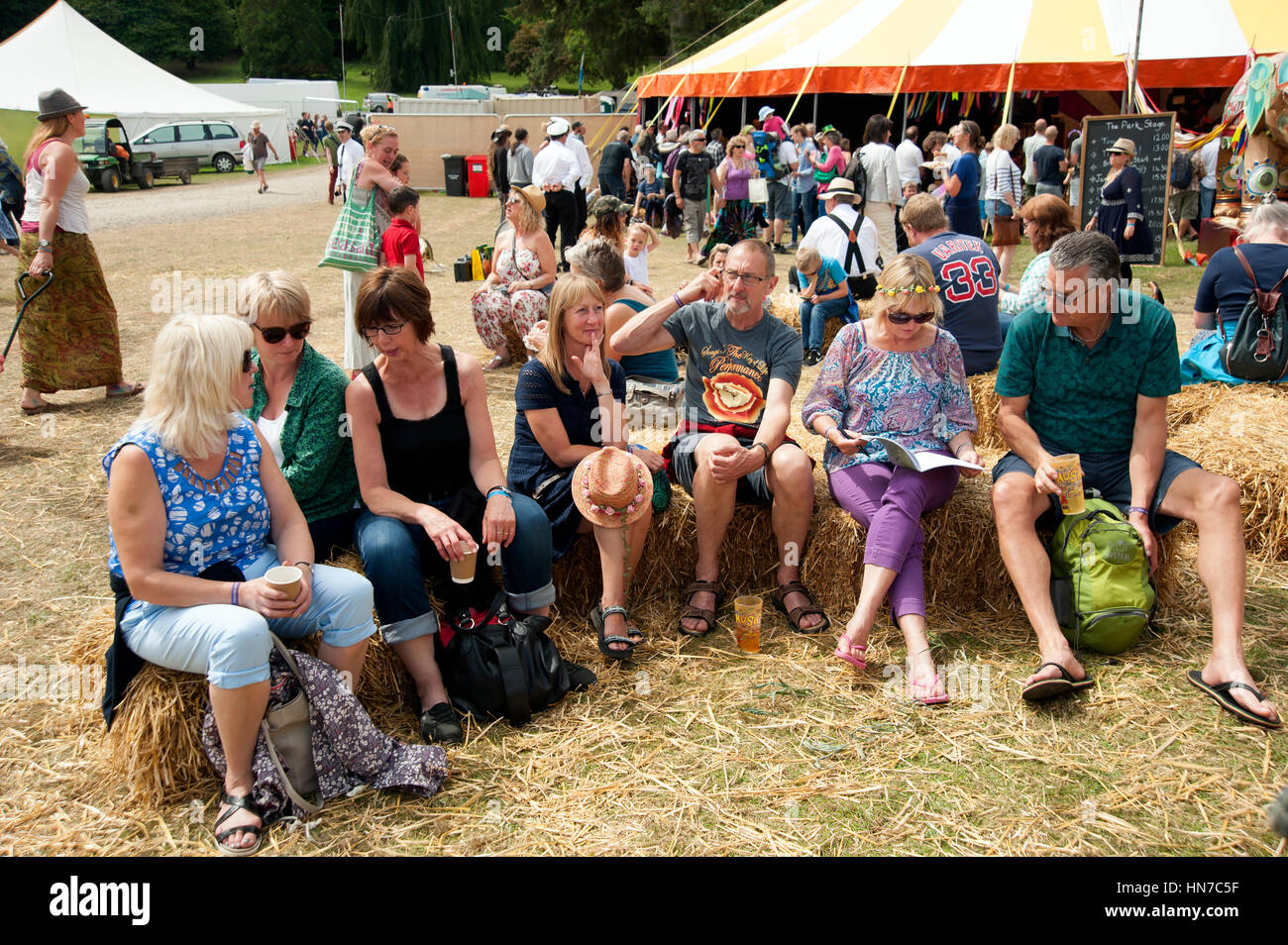 Un groupe de personnes d'âge moyen des couples assis sur des bottes de foin de boire une bière au Port Eliot Cornwall Festival Banque D'Images