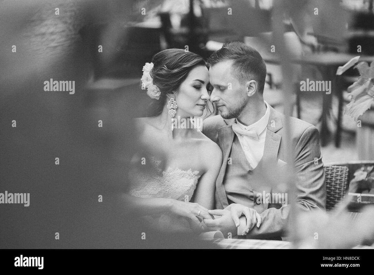 Heureux couple kissing while sitting in street cafe. La mariée et le marié dans un café, man hugging woman, woman. Voir au vert Banque D'Images