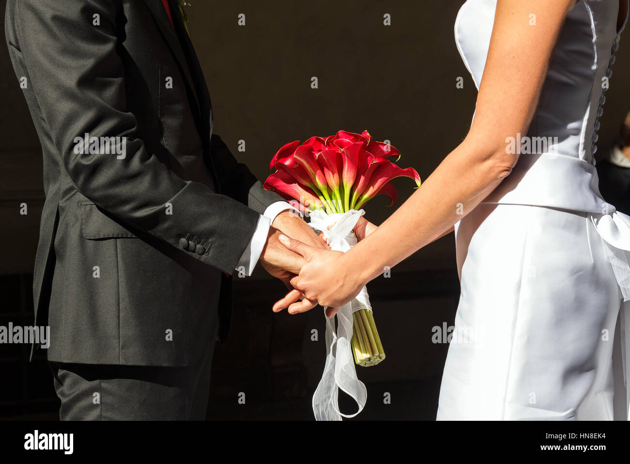 Les mains de la jeunes mariés sont entrelacés touch d'un bouquet de fleurs rouges Banque D'Images