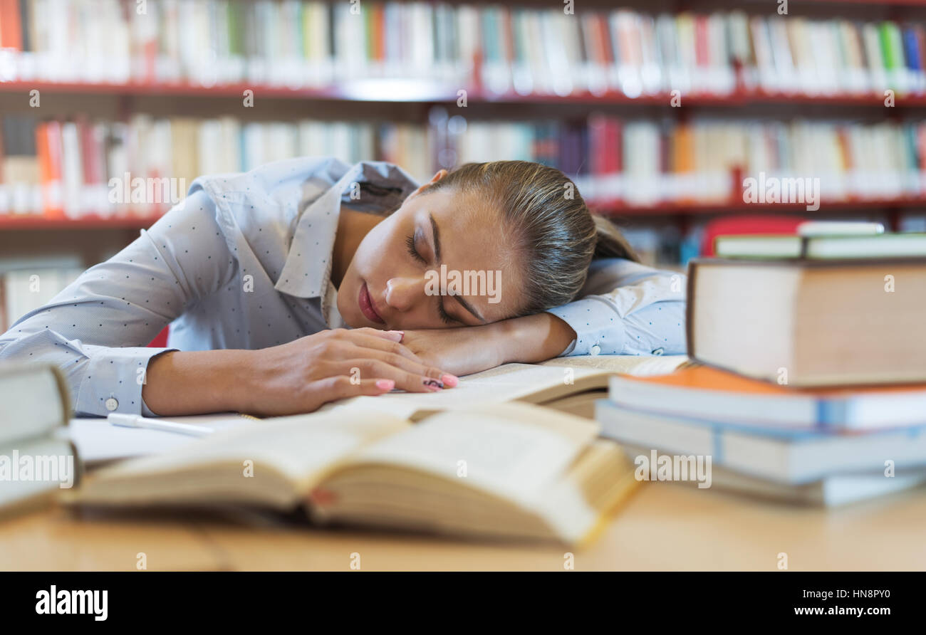 Fille étudiante étudier à la bibliothèque, elle est appuyée sur le bureau et de dormir, l'épuisement et la fatigue concept Banque D'Images