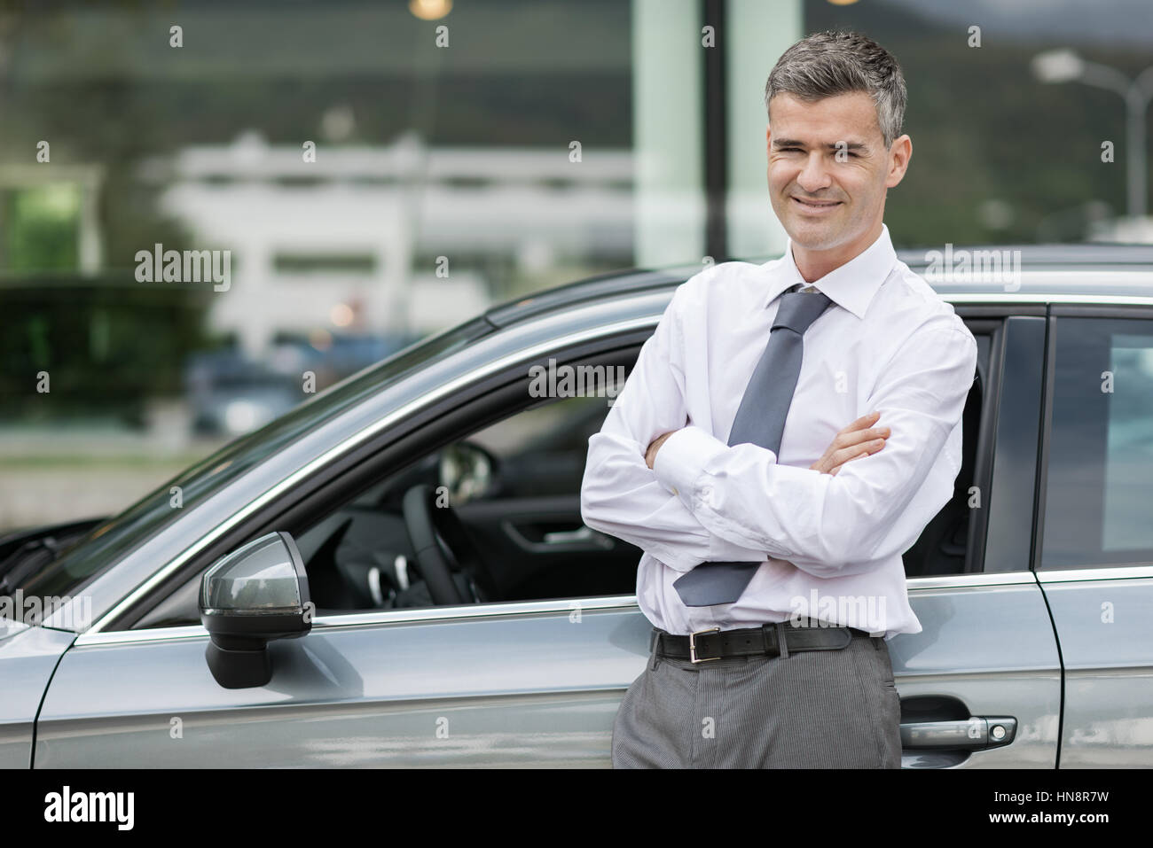 Businessman smiling at camera et appuyé contre sa voiture, cher nouveau concessionnaire et concept d'entreprise Banque D'Images
