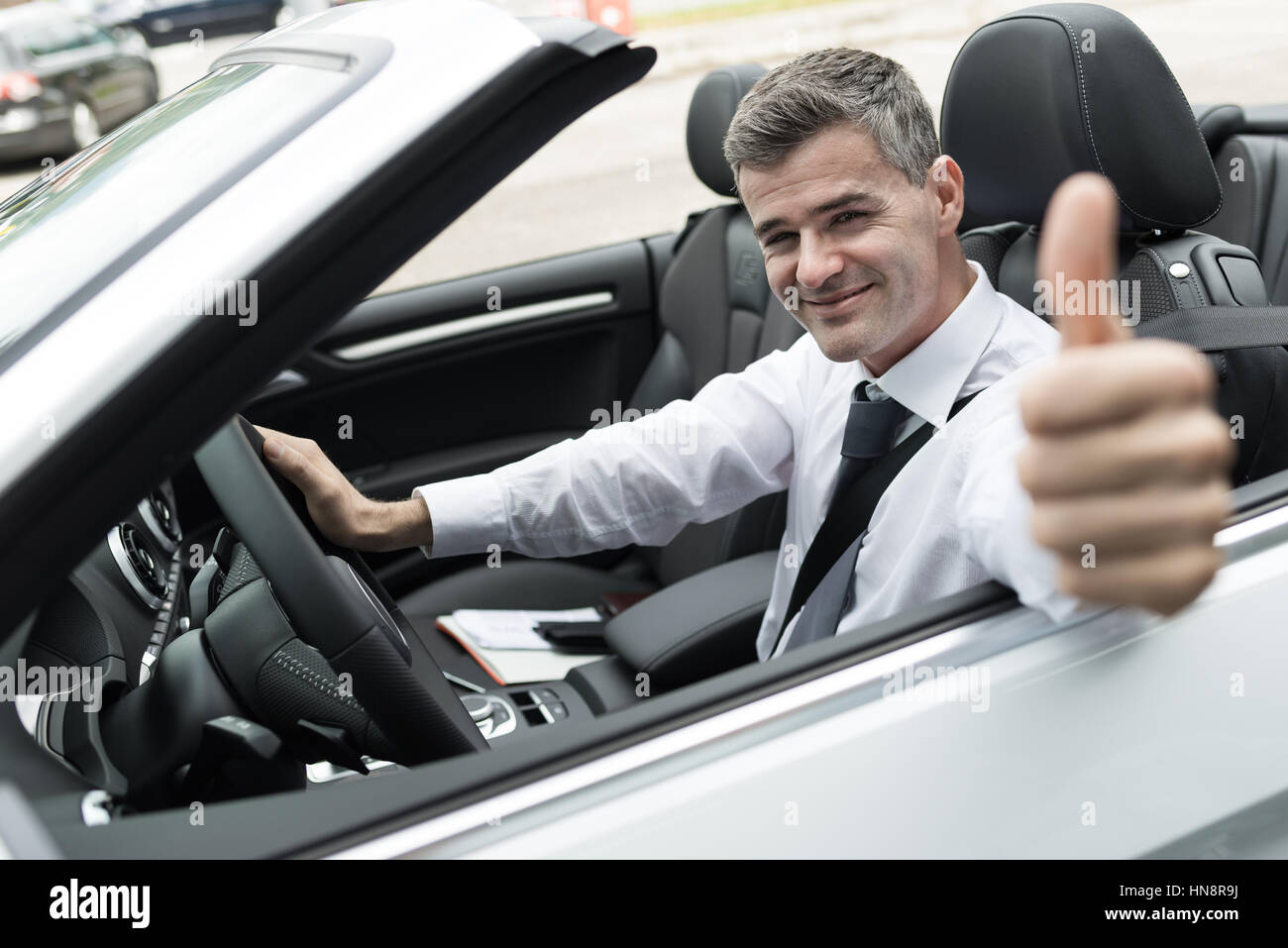 Succès sourire homme conduisant sa nouvelle voiture chère et donnant un Thumbs up Banque D'Images