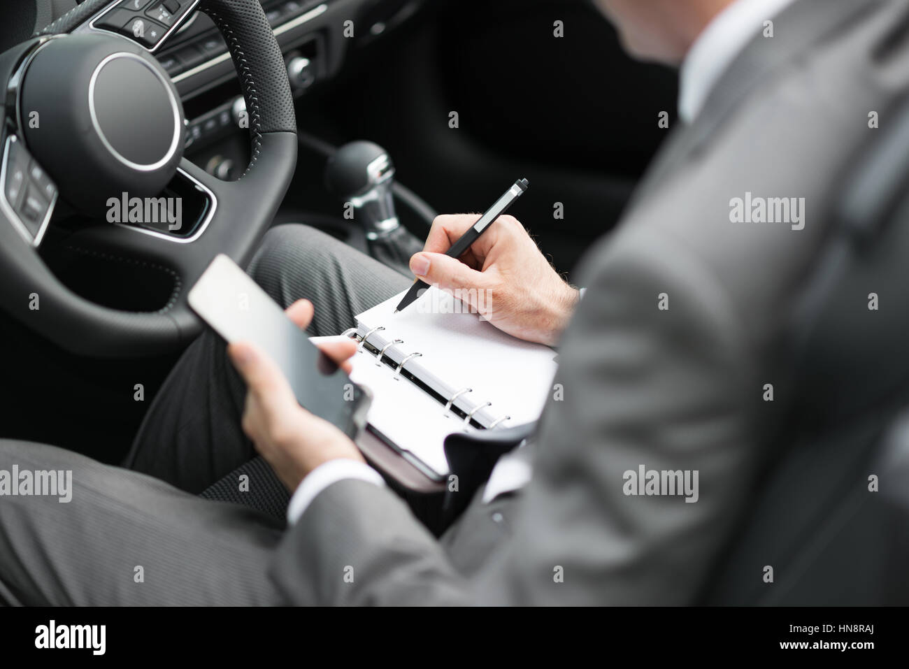 Portrait dans sa voiture, il est la planification et l'échéancier des réunions sur son organisateur et utiliser des applications sur son smartphone Banque D'Images