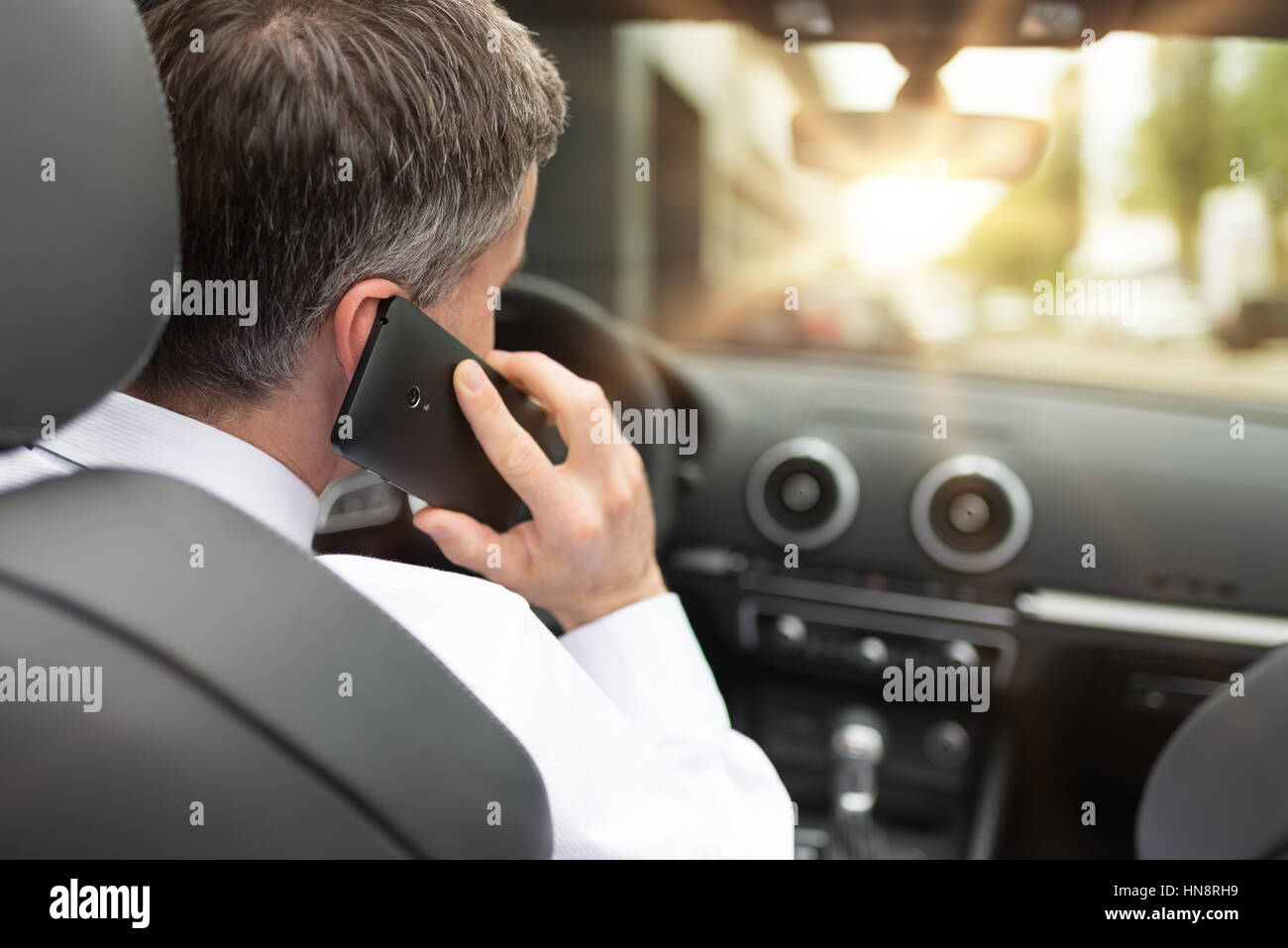 Manager au volant de sa voiture de luxe et avoir des appels professionnels avec son smartphone, vue arrière Banque D'Images