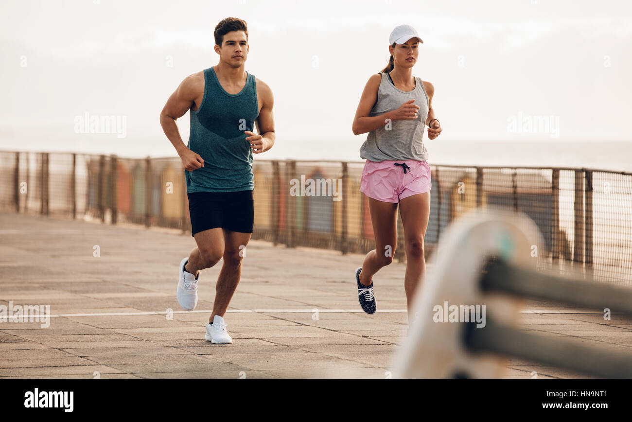 Deux coureurs courant le long de la route par la mer. fitness couple jogging sur la promenade du bord de mer. Banque D'Images