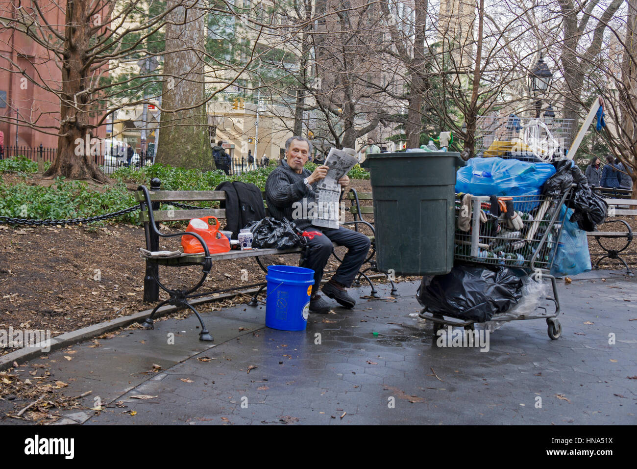Un homme qui semble être une personne de la rue avec ses biens et lire un journal. Dans la région de Washington Square Park à Greenwich Village, New York City. Banque D'Images