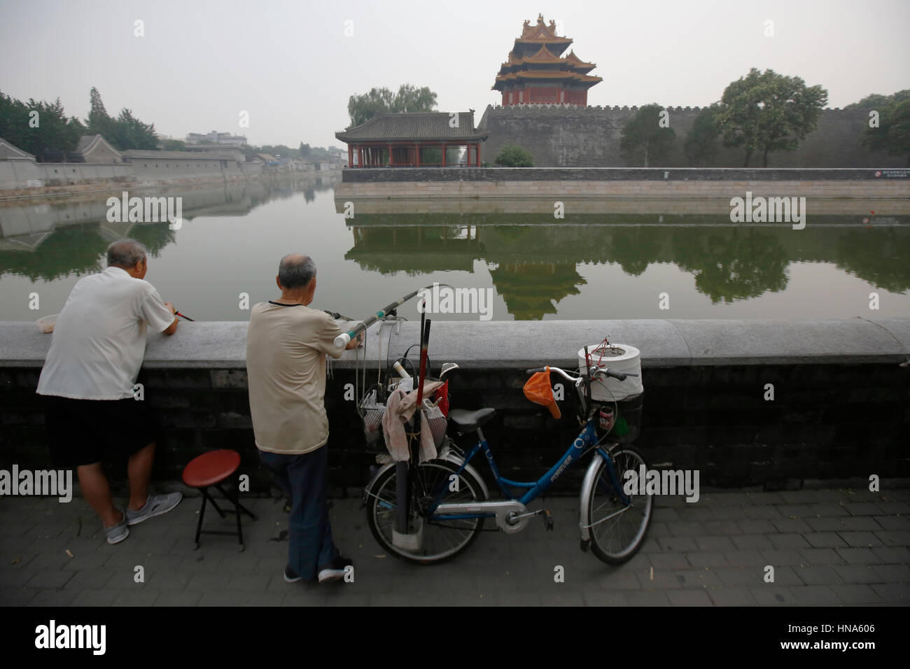 Les hommes pêchent en face de la Cité Interdite, qui se reflète dans les douves, ciel voilé en raison de la pollution, à Beijing, Chine, vendredi 29 juillet, 2016 Photographie : © Luc MacGr Banque D'Images